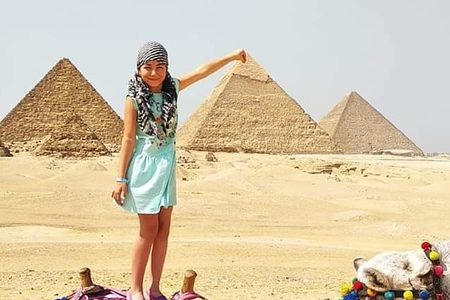 Young girl in a teal dress posing on a colourfully decorated camel with the Giza pyramids behind her