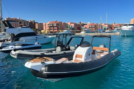 Private black RIB speedboat moored in a turquoise marina with colorful buildings and white yachts, Hurghada
